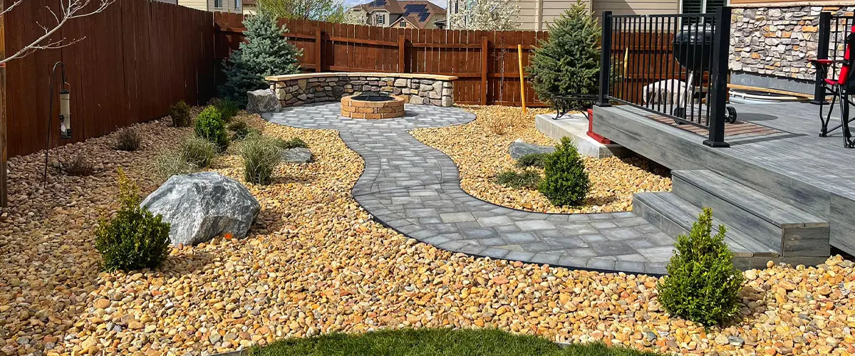 Backyard landscaping with stone fire pit, paver walkway, and decorative rock mulch by Easy Green Landscaping.