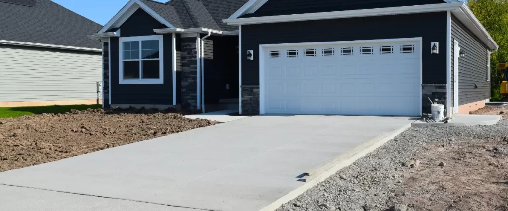 Modern concrete driveway in front of a black house with white garage door.