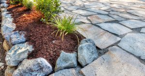 A modern raised garden bed with neat stone paving and dark brown mulch, featuring clean lines created by corten steel edging ideas for landscaping.