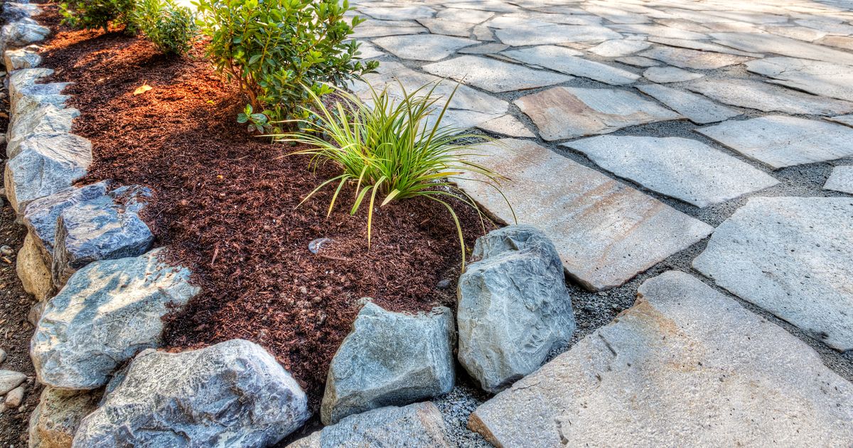 A modern raised garden bed with neat stone paving and dark brown mulch, featuring clean lines created by corten steel edging ideas for landscaping.