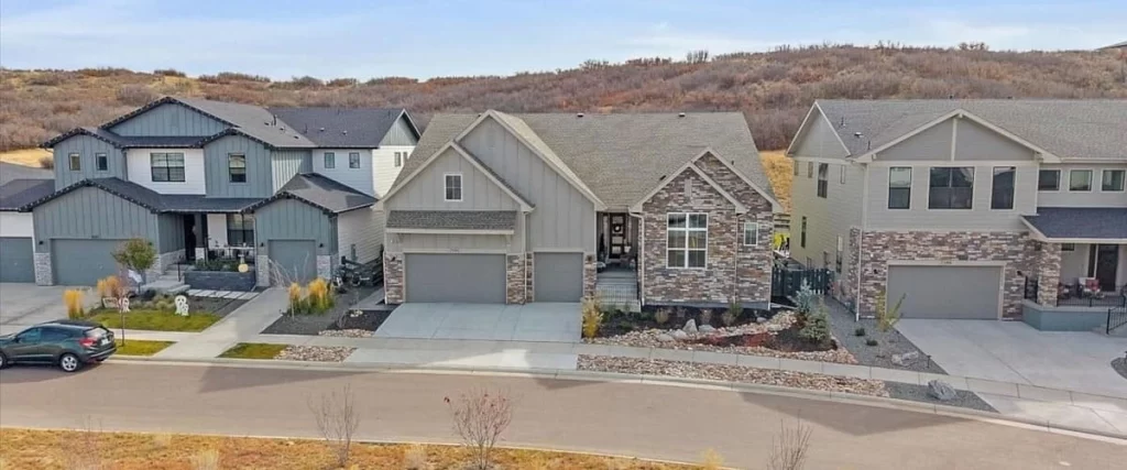 An elevated street view of luxury Toll Brothers At The Canyons homes in Castle Pines, CO, featuring modern craftsman architecture with stone accents, neutral siding, and landscaped front yards under a clear sky.