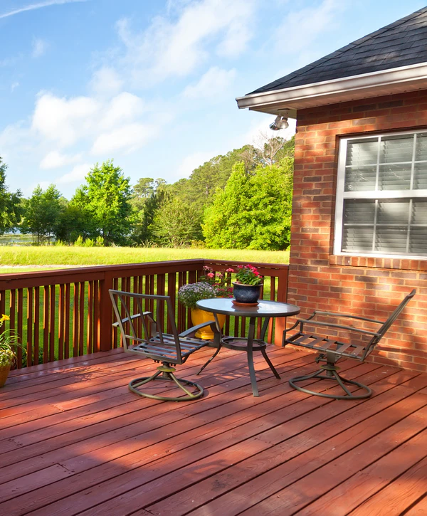 A beautiful reddish-wood deck installation on a brick home in Centennial, CO, featuring a black metal patio dining set overlooking a green backyard.