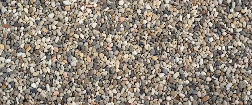 A close-up view of smooth, multi-colored pea gravel showing varied natural shades of grey, tan, and white.