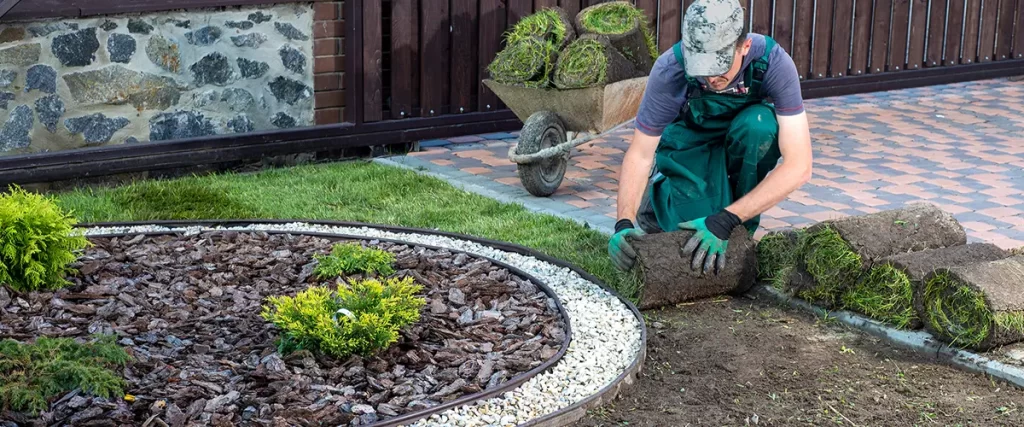 Landscaping contractor installing new sod around a garden bed for a healthy residential lawn.